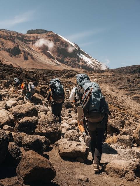 Trekkers carrying backpacks along a rocky Mount Kilimanjaro trail